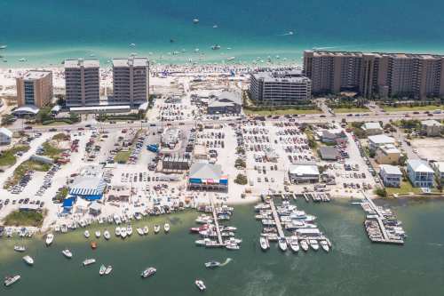 Aerial view of a beach area with boats, parking lots, and high-rise buildings along the coastline.
