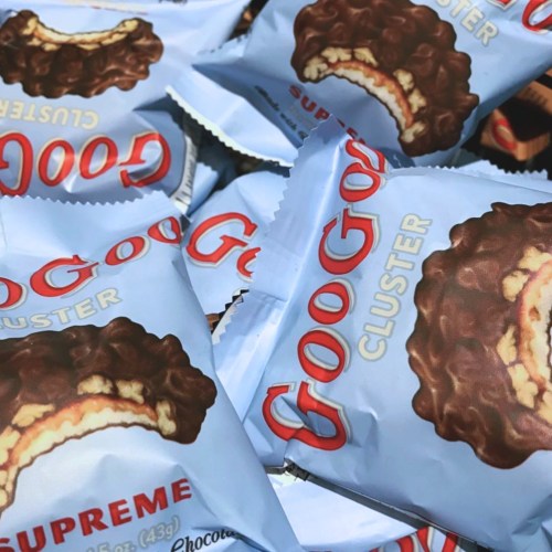 A close-up of multiple packages of Goobers Cluster candy, featuring a chocolate-covered treat with a creamy filling.