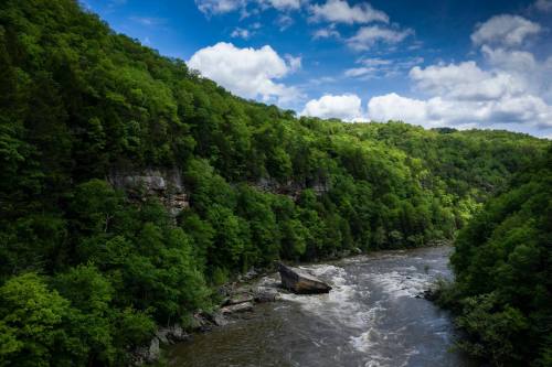 A serene river flows through lush green hills under a partly cloudy sky.