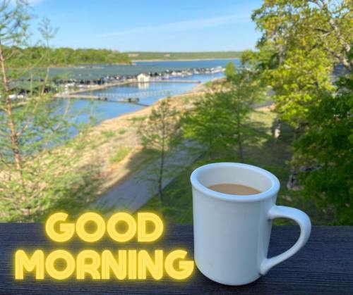 A white coffee mug sits on a railing with a scenic view of a marina and trees, accompanied by the text "GOOD MORNING."