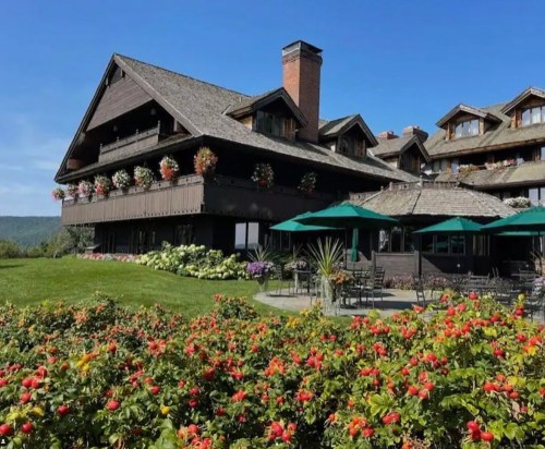 A charming lodge surrounded by vibrant flowers and green lawns under a clear blue sky.