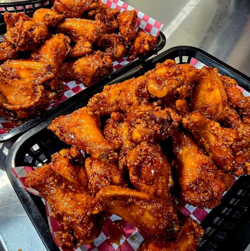 Two baskets of crispy, saucy chicken wings with a glossy finish, lined with red and white checkered paper.