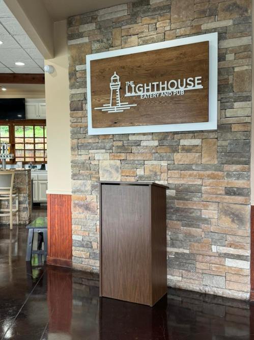 A wooden podium in front of a stone wall featuring a sign for "The Lighthouse Eatery and Pub."
