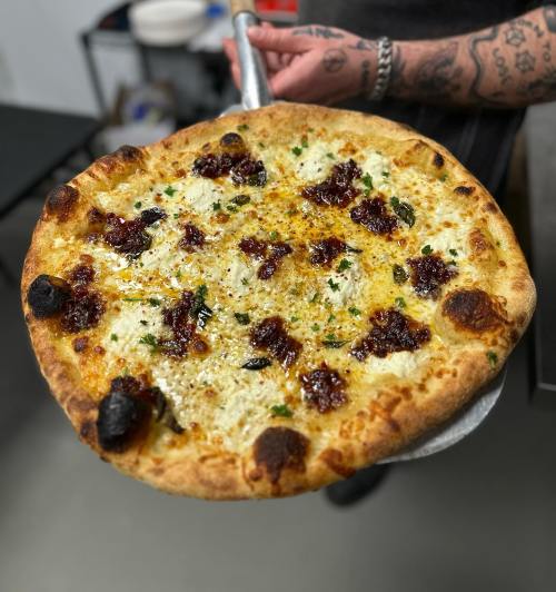 A freshly baked pizza with a golden crust, topped with cheese, herbs, and dark red sauce, held on a pizza peel.