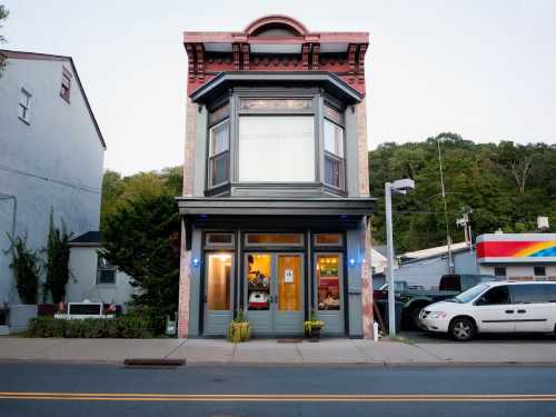 A charming two-story building with large windows, surrounded by trees and parked cars, in a small town setting.