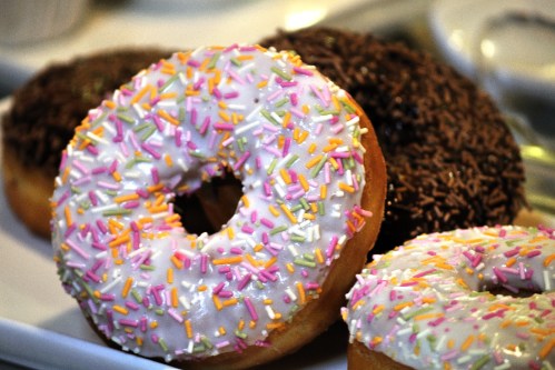 A close-up of three donuts: one with pink icing and sprinkles, one with chocolate icing, and one plain.