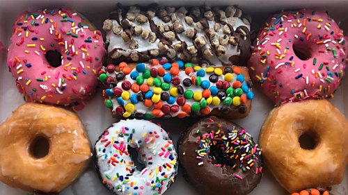 A box of colorful donuts, featuring sprinkles, chocolate, and candy toppings, arranged in a tempting display.