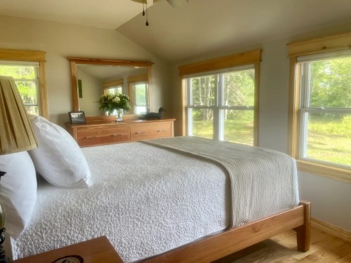 Cozy bedroom with a wooden bed, white bedding, and large windows overlooking a green landscape.