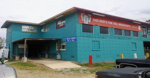 A turquoise building with a red sign reading "THIS BUD'S FOR YOU, MISSISSIPPI," featuring a bar and grill entrance.