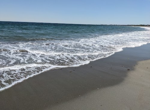 Waves gently lapping at a sandy beach under a clear blue sky.