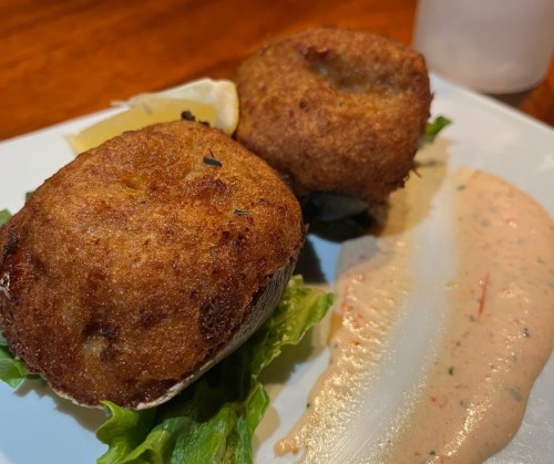 Two golden-brown crab cakes on a bed of lettuce, served with a creamy sauce and lemon wedges on the side.