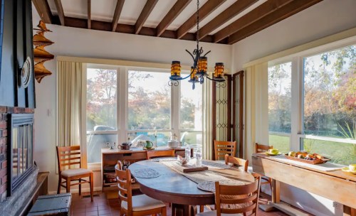Cozy dining area with wooden table, chairs, and large windows showcasing a scenic outdoor view.