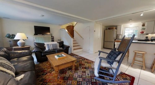 Cozy living room with a leather sofa, wooden coffee table, and a staircase, featuring a TV and a rocking chair.