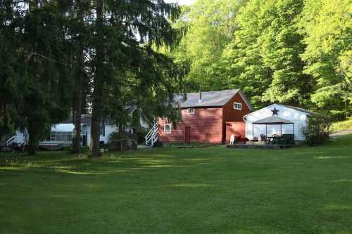 A scenic view of a red barn and white house surrounded by lush green trees and a grassy lawn.