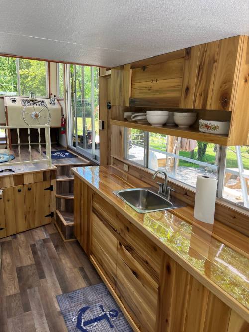 A modern kitchen with wooden cabinets, a sink, and large windows overlooking a green outdoor area.