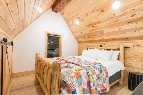 Cozy bedroom with a wooden ceiling, log bed, and colorful quilt, featuring natural light and a rustic design.