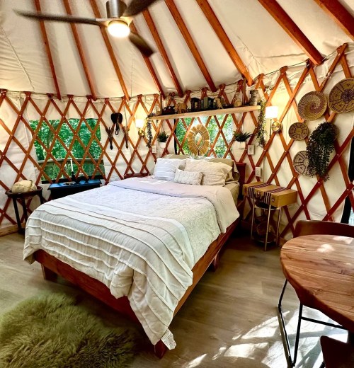 Cozy yurt interior featuring a bed, wooden furniture, and decorative wall hangings in a natural setting.