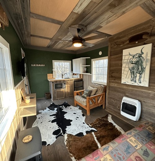 Cozy interior of a rustic cabin featuring a cowhide rug, wooden furniture, and a small kitchenette.
