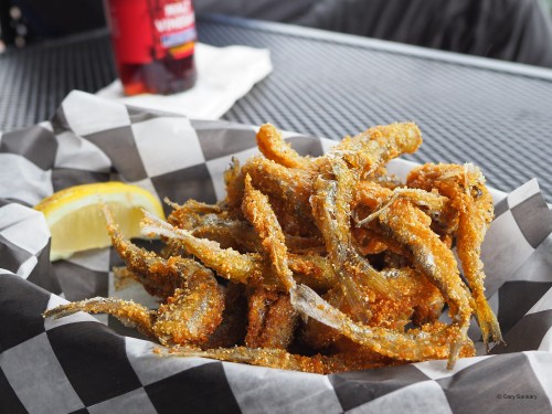 A plate of crispy fried fish served with a lemon wedge, on a checkered paper background.