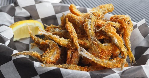 A basket of crispy fried fish with a lemon wedge, served on black and white checkered paper.