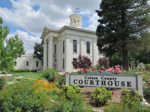 Colusa County Courthouse surrounded by colorful flowers and greenery under a partly cloudy sky.