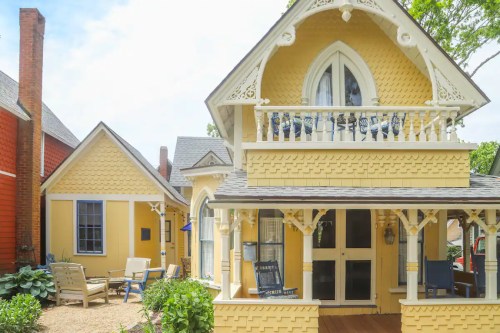 A charming yellow house with intricate details, a porch, and outdoor seating surrounded by greenery.