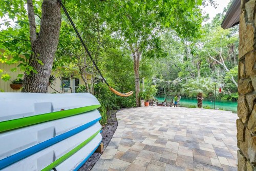 A serene outdoor space with kayaks, a hammock, and a patio overlooking a lush green river.