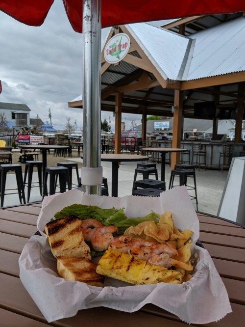 A plate with grilled shrimp, lettuce, grilled pineapple, and chips on a table, with an outdoor dining area in the background.