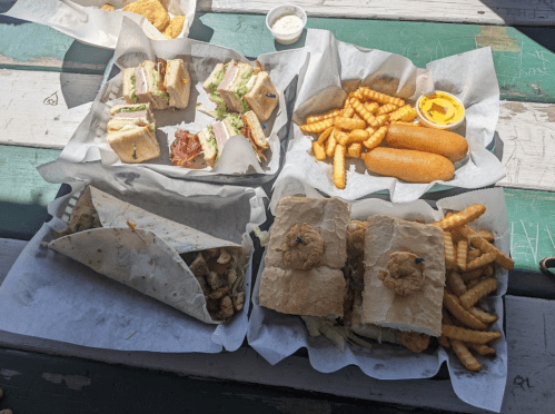 A spread of sandwiches, fries, and corn dogs on a table, with a side of dipping sauce.