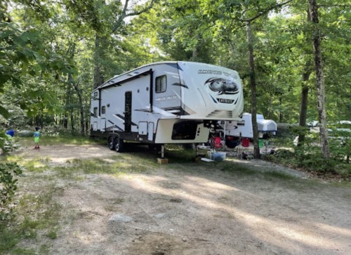 A large RV parked on a dirt path surrounded by trees in a wooded area.