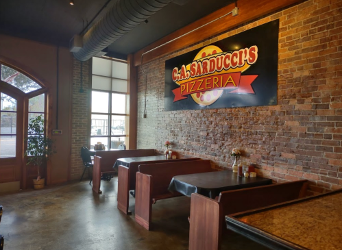Interior of C.A. Sarducci's Pizzeria featuring wooden booths and a large sign on a brick wall.