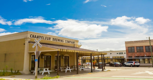 Exterior of Chandeleur Brewing Company with a clear blue sky and nearby buildings, including a coffee shop.