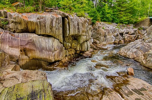 A rocky riverbed with flowing water surrounded by lush green trees and textured stone formations.