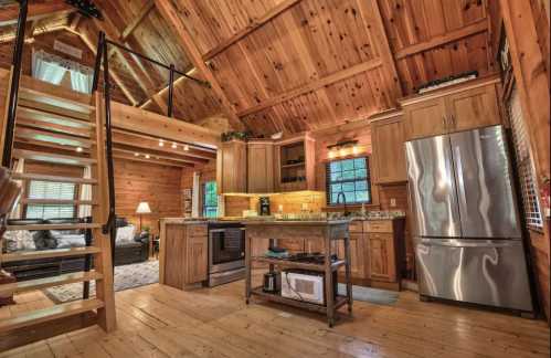 Cozy wooden kitchen with modern appliances, open layout, and a staircase leading to a loft area. Warm, inviting atmosphere.