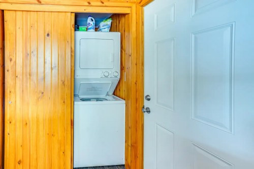 A laundry area featuring a stacked washer and dryer in a wooden-paneled room next to a closed door.