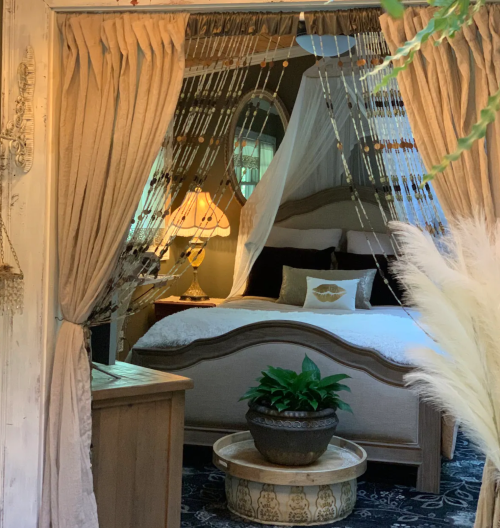 Cozy bedroom with a canopy bed, soft lighting, and decorative curtains, featuring a potted plant and elegant decor.