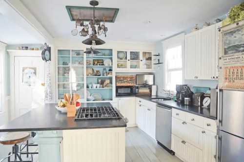 Bright kitchen with white cabinets, a central island, and open shelves displaying dishes and decor. Modern appliances included.