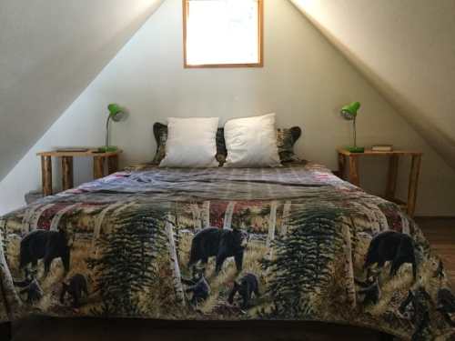 Cozy attic bedroom with a bear-themed blanket, two green lamps, and a window letting in natural light.