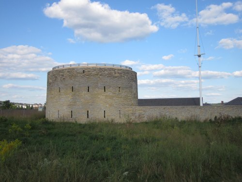 A round stone tower surrounded by grass under a blue sky with clouds. A flagpole stands nearby.