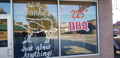 Window display featuring a cow graphic and text: "We'll smoke BBQ 225° etc. Just about Anything!"
