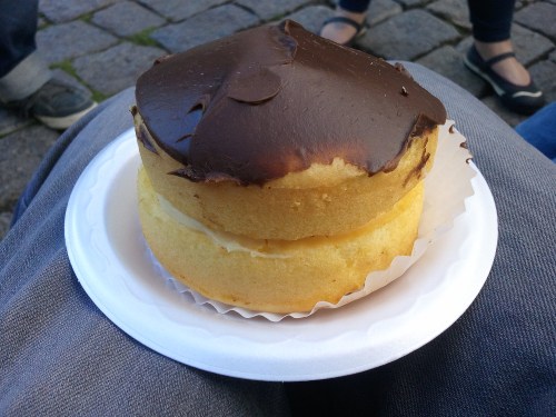 A round cake with a chocolate frosting top and a creamy filling, served on a white paper plate.