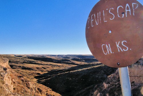 Sign for Devil's Gap in Kansas, overlooking a vast, rugged landscape under a clear blue sky.