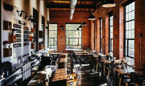 A spacious, modern restaurant with large windows, exposed brick walls, and wooden tables.