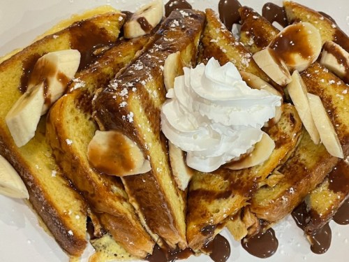 A plate of French toast topped with banana slices, chocolate sauce, and whipped cream.