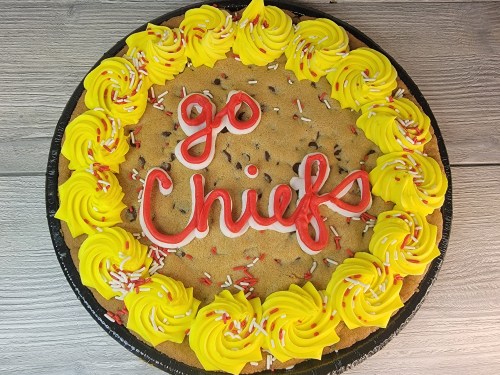 A large cookie cake decorated with yellow frosting swirls and red lettering that says "go Chiefs," with colorful sprinkles.