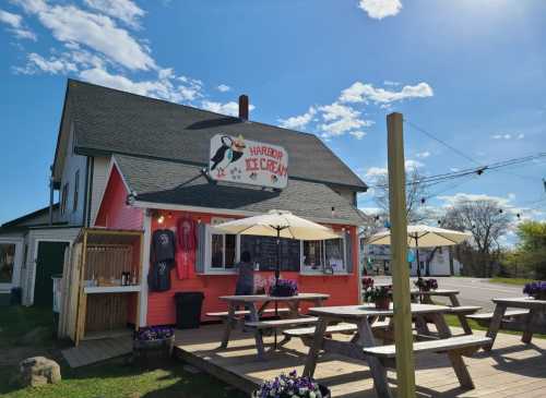 A colorful ice cream shop with outdoor seating, umbrellas, and a sign featuring a cow, set against a clear blue sky.