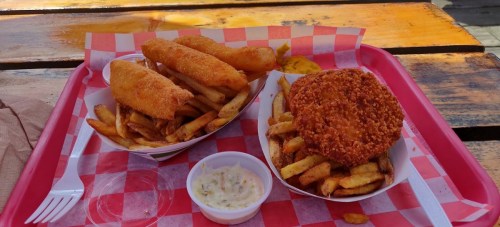 Two trays of food featuring fried fish, chicken, and a generous serving of French fries, with a side of dipping sauce.