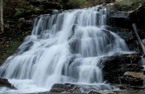 A serene waterfall cascading over rocky steps, surrounded by lush greenery and natural scenery.