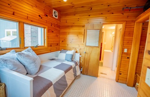 Cozy wooden room with a daybed, large windows, and a door leading to a bathroom. Warm, inviting atmosphere.