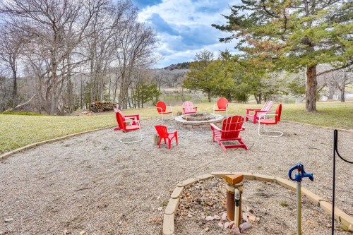 A circular fire pit area with red chairs surrounded by trees and a grassy landscape under a cloudy sky.